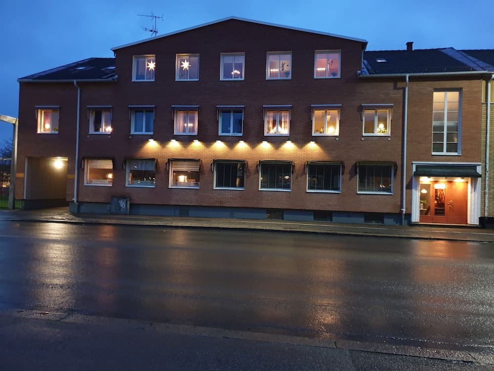 A cozy evening scene captures a warmly lit brick building with festive window decorations, ideal for travelers seeking a charming urban stay during the holiday season.