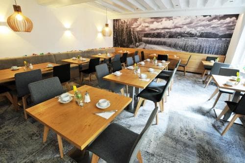 A cozy restaurant interior features wooden tables set for dining under warm pendant lights, with a mural of a serene landscape enhancing the inviting atmosphere, perfect for travelers seeking a comfortable spot to enjoy a meal.