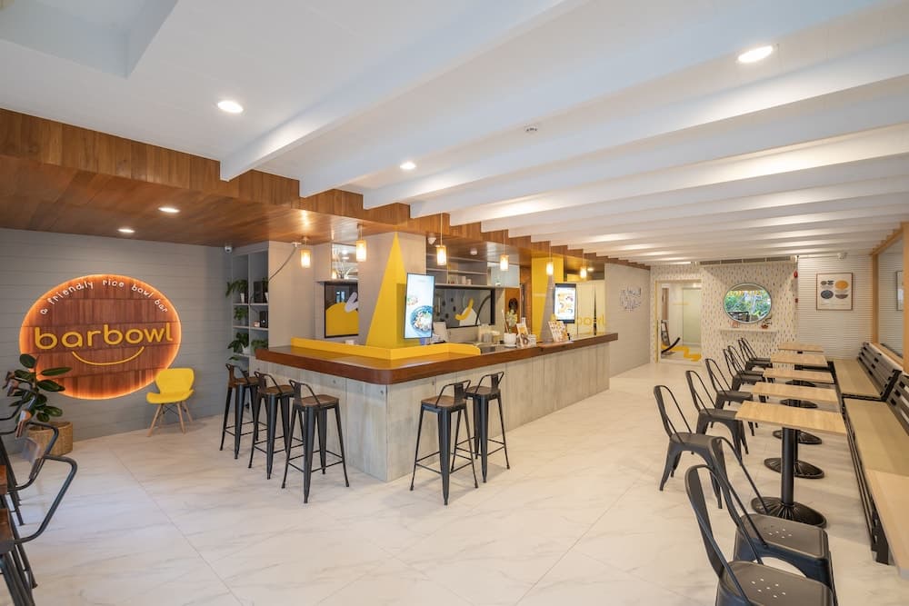 A bright and inviting modern café features sleek bar seating, minimalist tables, and vibrant yellow accents, ideal for travelers seeking a cozy spot to enjoy a meal or work remotely.