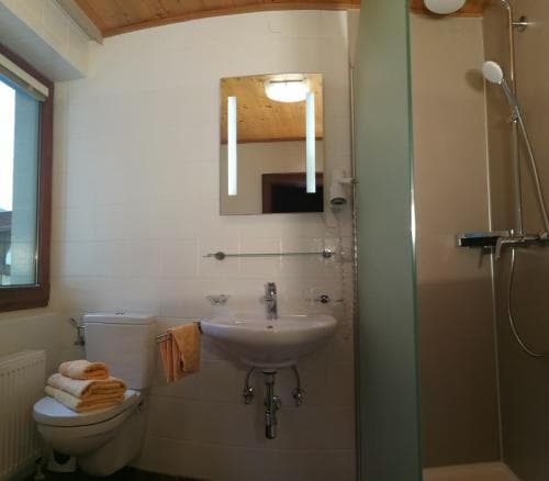 A cozy bathroom with white tiled walls, a sink, toilet, glass shower enclosure, and a window letting in natural light, ideal for travelers seeking comfort and cleanliness in their accommodations.