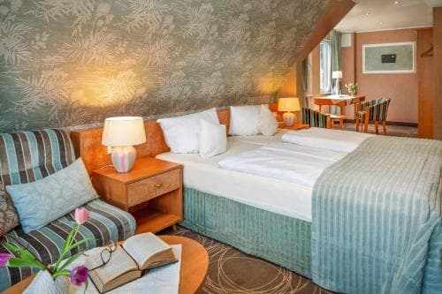 A cozy hotel room with a sloped ceiling, floral wallpaper, and neatly arranged furniture creates a warm and inviting atmosphere, perfect for travelers seeking comfort and relaxation.
