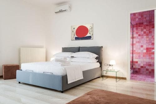 A serene hotel bedroom features a neatly made bed, vibrant red artwork, and a mosaic-tiled bathroom visible through an open door, ideal for travelers seeking modern comfort and style.