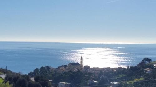 A serene coastal village with a prominent church spire overlooks the shimmering sea under a clear blue sky, ideal for tranquil seaside retreats and spiritual reflection.