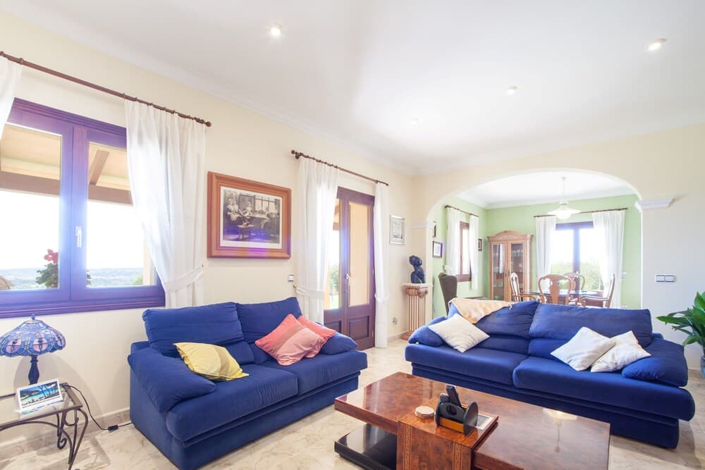 A cozy living room with vibrant blue sofas, framed artwork, and large windows offering scenic views, ideal for travelers seeking a comfortable and inviting vacation rental space.