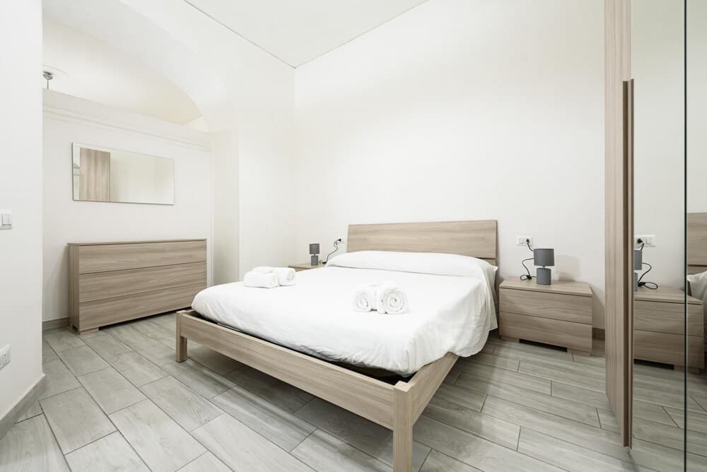 A serene minimalist bedroom with white linens, wooden furniture, and soft lighting creates an inviting atmosphere ideal for travelers seeking a cozy and tranquil accommodation experience.