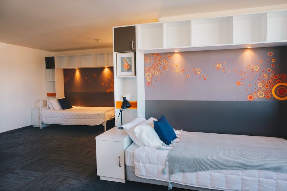 A cozy hotel room features two neatly made beds with vibrant orange circular wall art, modern shelving, and ambient lighting, ideal for travelers seeking comfort and style.