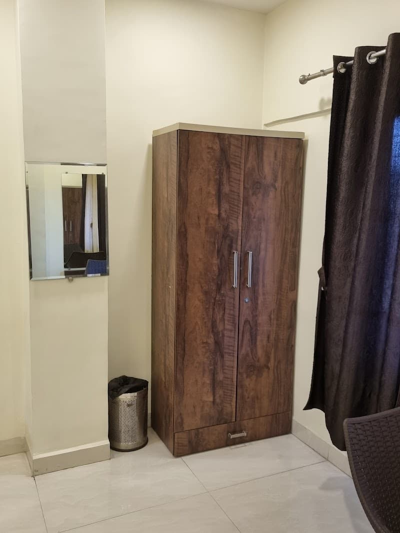 A cozy living space in Pune featuring a wooden wardrobe, a mirror, a trash bin, and a curtain, ideal for travelers seeking comfortable accommodations near the bus stand.