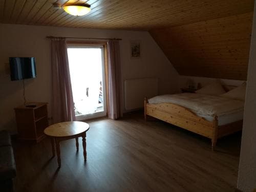 A cozy attic bedroom with wooden ceilings, a bright window, and simple furnishings offers a serene retreat for travelers seeking a peaceful stay.