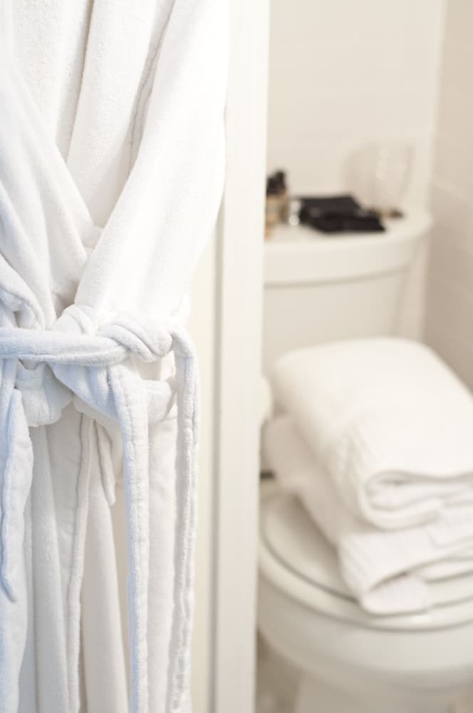 A serene hotel bathroom scene features a plush white robe hanging beside a neatly stacked towel on the toilet lid, ideal for travelers seeking comfort and relaxation.