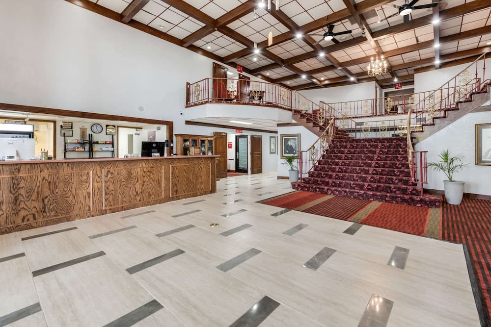 A grand hotel lobby features a polished marble floor, a wooden reception desk, a majestic staircase with red carpeting, and a warm, inviting atmosphere ideal for travelers seeking luxury accommodations.