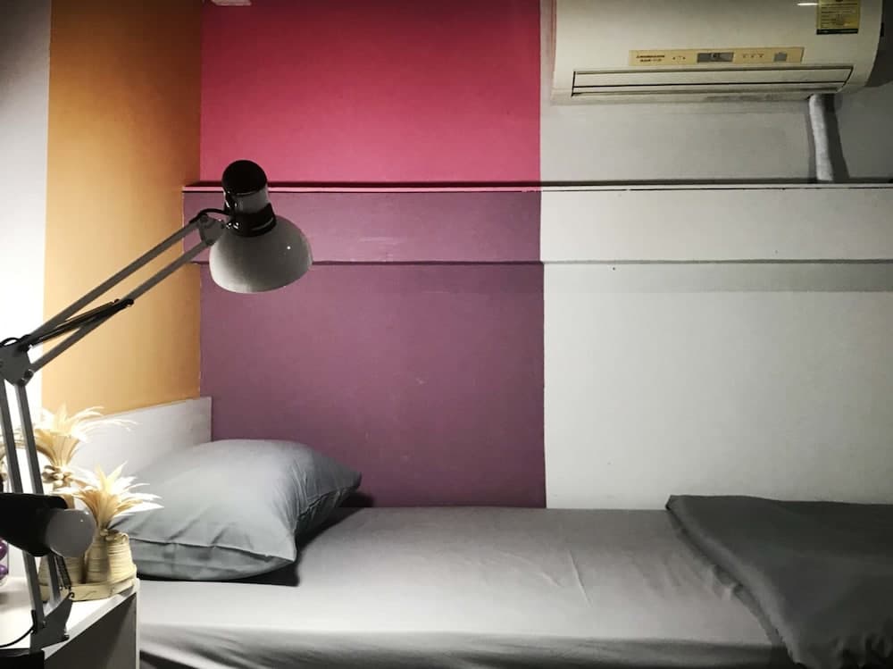 A cozy hostel room features a neatly made bed against a colorful geometric wall, illuminated by a desk lamp, ideal for budget travelers seeking comfort and style.