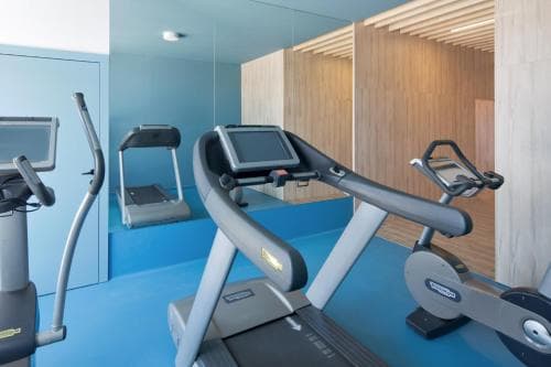 A modern gym with blue flooring, wooden paneling, and various cardio machines offers a serene workout environment ideal for travelers seeking fitness facilities during their stay.