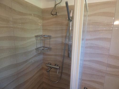 A modern bathroom features a sleek walk-in shower with wave-patterned tiles, a glass door, and a metal shelf, ideal for travelers seeking comfort and style in accommodations.