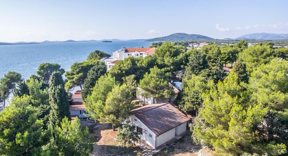 An aerial view of a serene coastal village nestled among lush green trees, with white-roofed houses overlooking the tranquil sea, ideal for travelers seeking a peaceful seaside retreat.