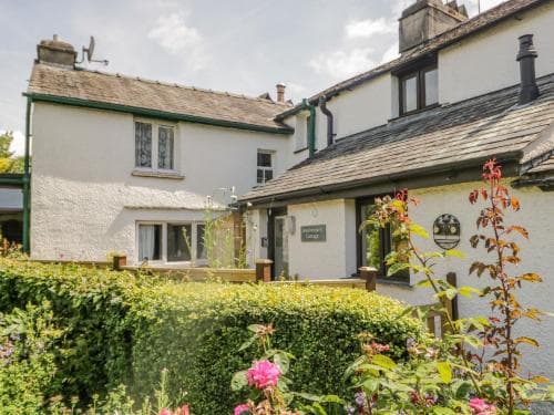 A charming white cottage with lush greenery and blooming flowers exudes a cozy, inviting atmosphere, perfect for a tranquil countryside getaway.