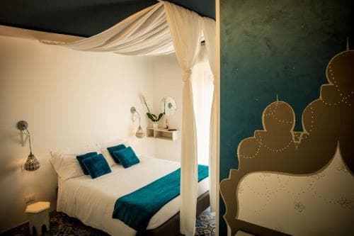 A cozy bedroom with a canopy bed draped in white fabric, teal accents, and a whimsical mural of a cityscape, evokes a serene and artistic atmosphere ideal for boutique hotel stays.