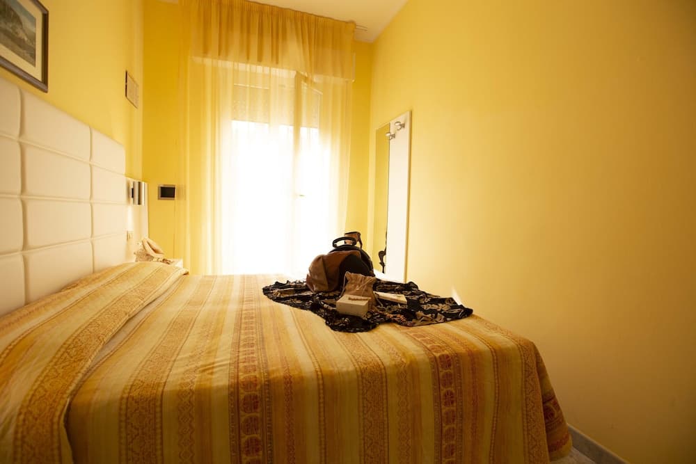 A cozy hotel room with yellow walls, a neatly made bed adorned with striped bedding, and soft sunlight filtering through sheer curtains creates a warm and inviting atmosphere ideal for travelers seeking relaxation.