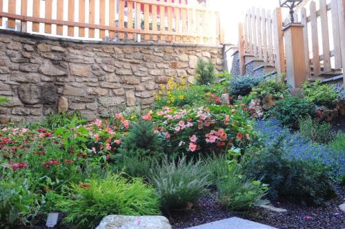 A vibrant garden with colorful flowers and lush greenery thrives beside a rustic stone wall and wooden fence, creating a serene suburban retreat ideal for nature lovers seeking peaceful outdoor spaces.