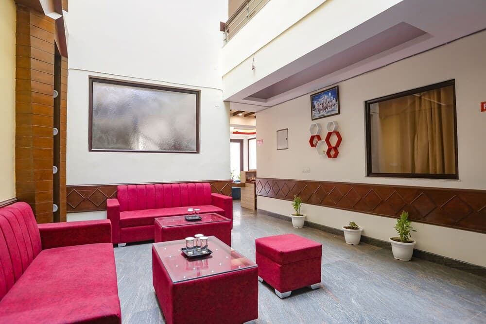A cozy hotel lobby features vibrant red seating, glass coffee tables, and potted plants against wooden-paneled walls, creating a welcoming atmosphere ideal for travelers seeking relaxation.