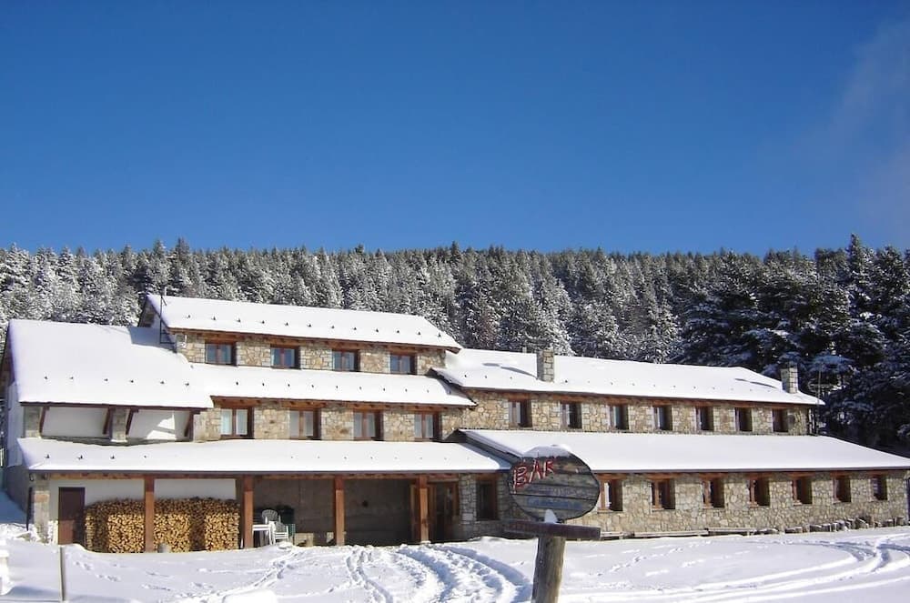 A serene winter retreat features a rustic stone lodge nestled in a snow-covered forest under a clear blue sky, ideal for travelers seeking cozy accommodations amidst nature's tranquility.