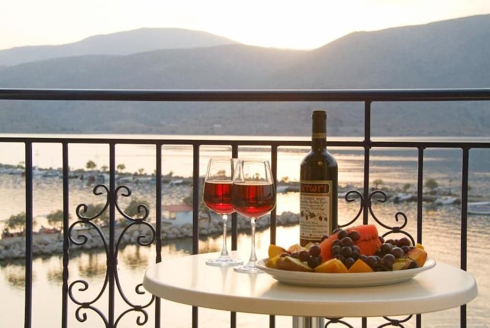 A serene balcony scene overlooking a tranquil harbor at sunset, featuring a table set with wine glasses, a bottle of wine, and a fruit platter, ideal for romantic getaways or leisurely travel experiences.