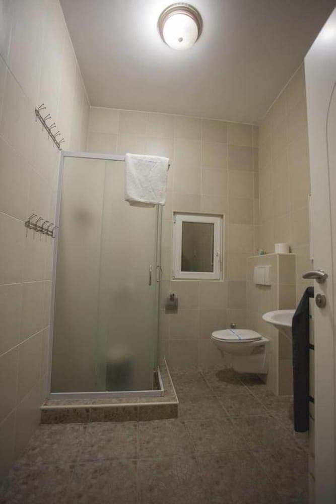 A clean, modern bathroom with beige tiles, a glass-enclosed shower, wall-mounted toilet, and sink offers a functional and cozy space ideal for travelers seeking comfort in accommodations.