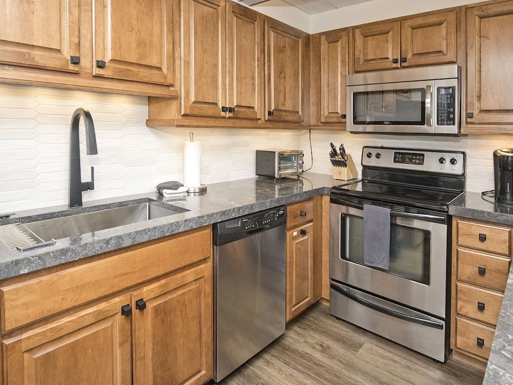 A cozy kitchen with wooden cabinets, stainless steel appliances, and a modern backsplash offers a warm and inviting atmosphere ideal for travelers seeking a homey cooking experience.