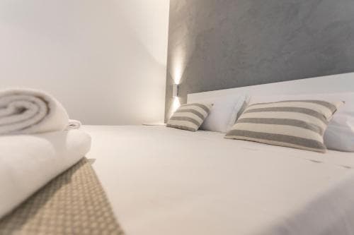 A serene minimalist bedroom with soft lighting, neatly arranged pillows, and folded towels on a textured bench, ideal for travelers seeking a tranquil and modern accommodation experience.