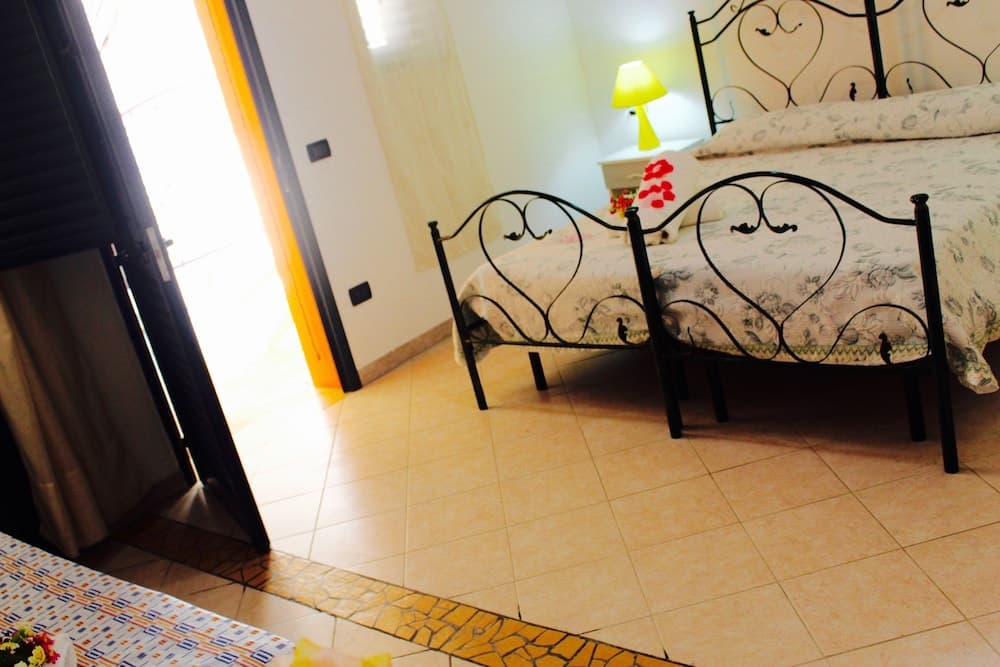 A cozy hotel room with heart-patterned wrought iron bed frames, tiled floors, and a bright doorway leading to natural light, ideal for travelers seeking a romantic and comfortable stay.