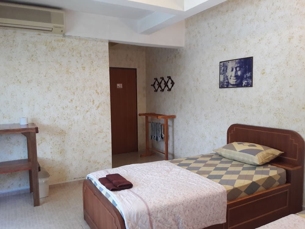 A cozy guesthouse bedroom with textured walls, wooden furniture, and neatly arranged bedding offers a serene retreat for travelers seeking simplicity and comfort.