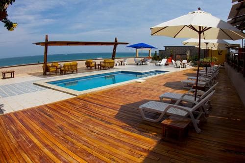 A serene rooftop poolside scene with wooden decking, lounge chairs, umbrellas, and ocean views offers an ideal spot for relaxation and leisure travel.