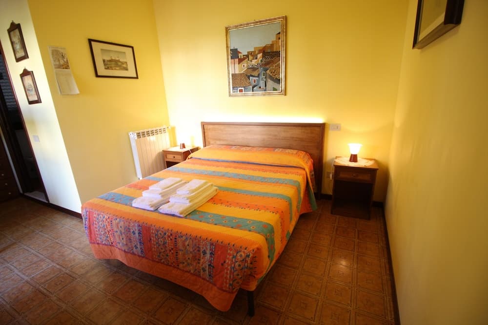 A cozy bedroom with yellow walls, wooden furniture, and vibrant bedding offers a warm and inviting atmosphere ideal for travelers seeking comfort in a quaint accommodation.