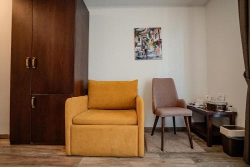 A cozy hotel room features a vibrant yellow armchair, a wooden desk with tea-making facilities, and a colorful wall art piece, creating a warm and inviting atmosphere ideal for travelers seeking comfort and relaxation.