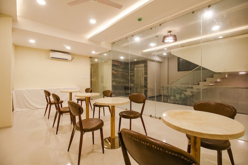 A cozy indoor café features round tables with leather chairs, glass partitions, and a staircase in the background, creating an inviting atmosphere ideal for travelers seeking a quiet spot to relax or work.