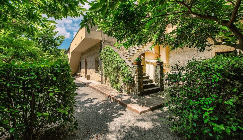 A serene courtyard surrounded by lush greenery frames a charming stone villa with a staircase, ideal for travelers seeking a peaceful retreat in a picturesque setting.