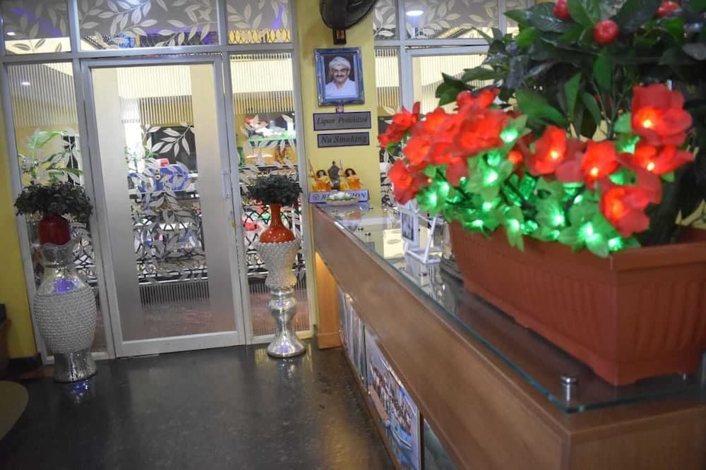 A warmly lit indoor reception area features decorative vases, a vibrant LED-lit flower arrangement, and framed notices, creating an inviting atmosphere for travelers seeking local services or accommodations.