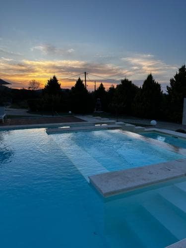 A serene sunset illuminates a tranquil poolside scene with clear blue water, surrounded by lush greenery, ideal for a relaxing vacation retreat.