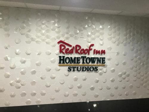 A modern interior wall adorned with geometric patterns features the "Red Roof Inn HOMETOWNE STUDIOS" sign, creating a professional ambiance ideal for business travelers seeking a stylish accommodation option.