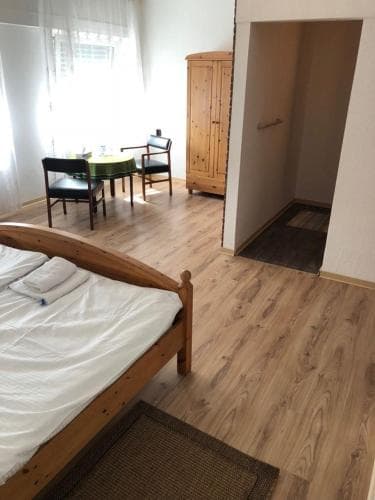 A cozy studio apartment features a neatly made bed, wooden flooring, a dining area with chairs and a table, and a wardrobe, ideal for travelers seeking a comfortable and functional stay.