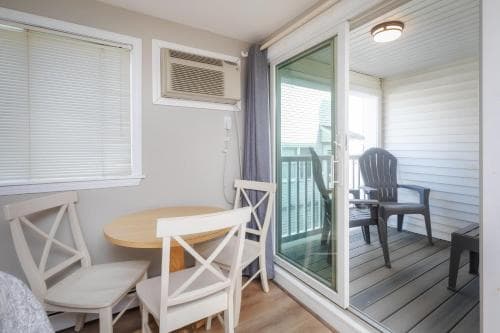 A cozy indoor dining nook with white chairs and a round table leads to a serene outdoor deck through a glass door, ideal for travelers seeking a relaxing retreat with easy access to fresh air and outdoor seating.