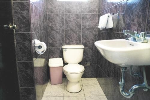 A compact bathroom with dark marble tiles, white fixtures including a toilet and sink, and a towel hanging on the wall offers a practical space for travelers seeking basic amenities.