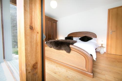 A cozy bedroom with wooden furnishings, a plush bed adorned with a fur throw, and soft lighting creates a serene retreat ideal for travelers seeking relaxation in a rustic lodge setting.