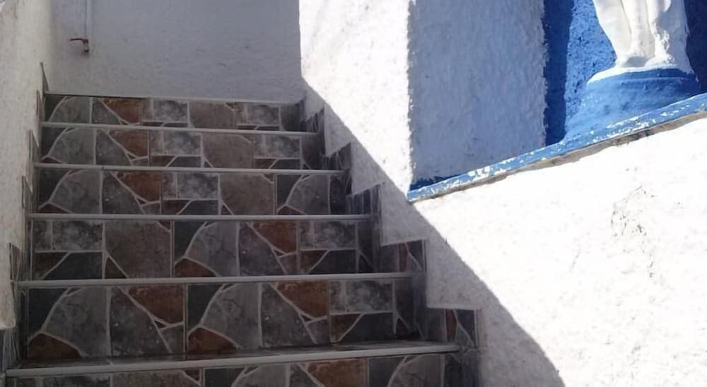 A serene outdoor staircase with mosaic tiles ascends beside a white wall adorned with blue trim and a statue, ideal for exploring cultural heritage sites.