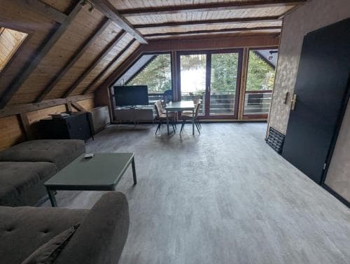 A cozy attic living space with wooden beams, modern furnishings, and large windows overlooking a serene snowy landscape, ideal for a relaxing winter getaway.