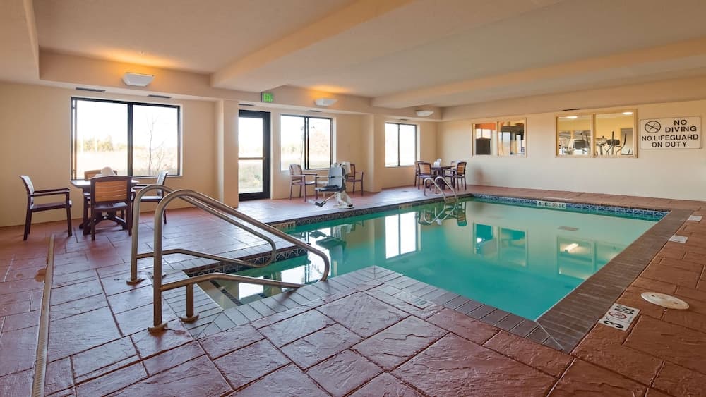 A serene indoor pool area with tiled floors, lounge seating, large windows, and a metal staircase offers a relaxing retreat for travelers seeking leisure and comfort.