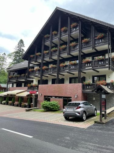 A charming multi-story lodge with balconies adorned with flowers stands invitingly amidst greenery, offering travelers a cozy retreat in a serene mountainous area.