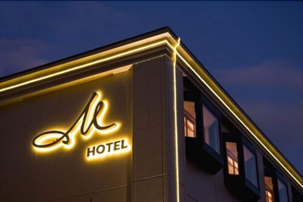 A modern hotel facade illuminated by warm neon lights at dusk, featuring a stylish "M Hotel" sign, creates an inviting atmosphere ideal for travelers seeking upscale accommodations.