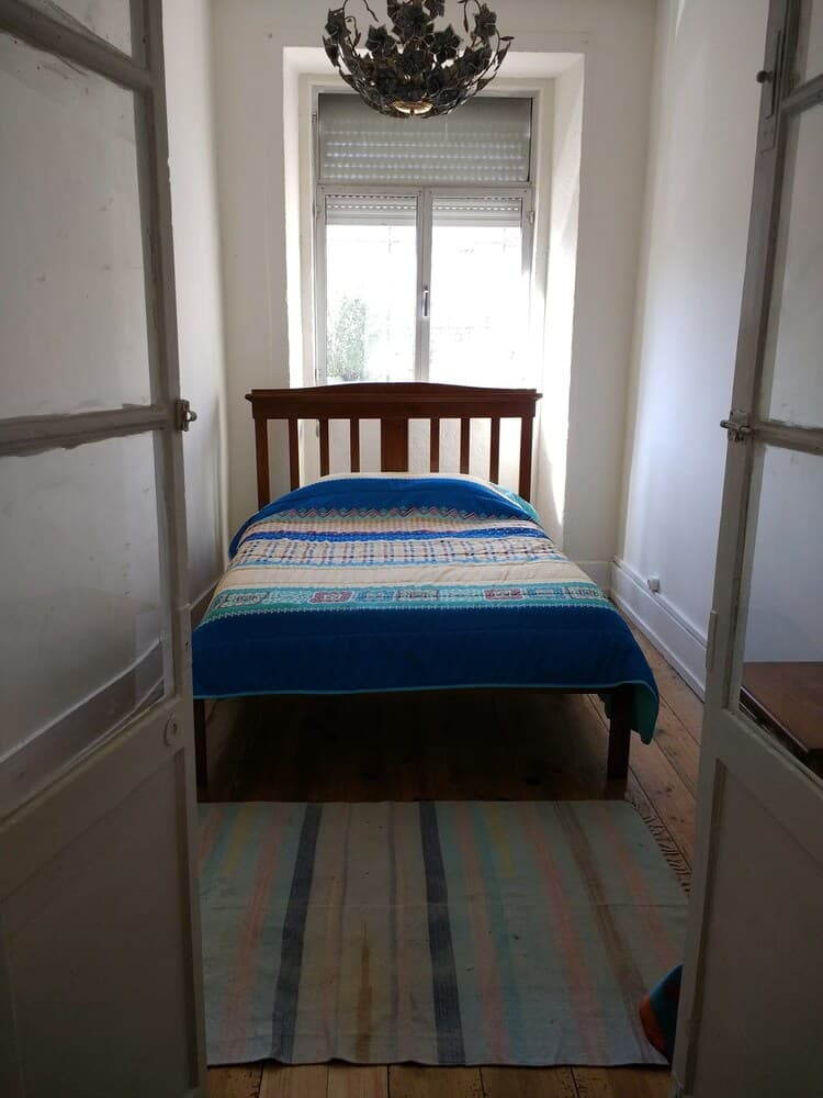 A cozy bedroom with a wooden bed adorned in colorful bedding, framed by open doors, features a striped rug and a chandelier, ideal for travelers seeking a quaint and charming accommodation.