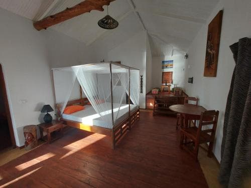 A cozy, rustic bedroom with wooden floors, a mosquito-netted bed, and warm lighting creates an inviting atmosphere ideal for travelers seeking a serene retreat in a tropical setting.