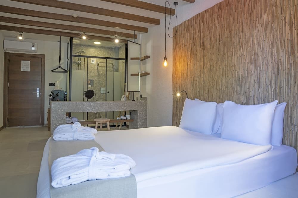 A cozy hotel room with a neatly made bed, bamboo wall decor, and an open bathroom view offers a serene retreat for travelers seeking relaxation.